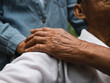 © scentrio - Close-up hand of granddaughter holding grandfather's shoulder in a wheelchair in the park. Family life on vacation.
