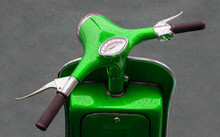 A Bright Green Motor Scooter Showing Front End From Riders View. The Paintwork Has Water Droplets From The Rain