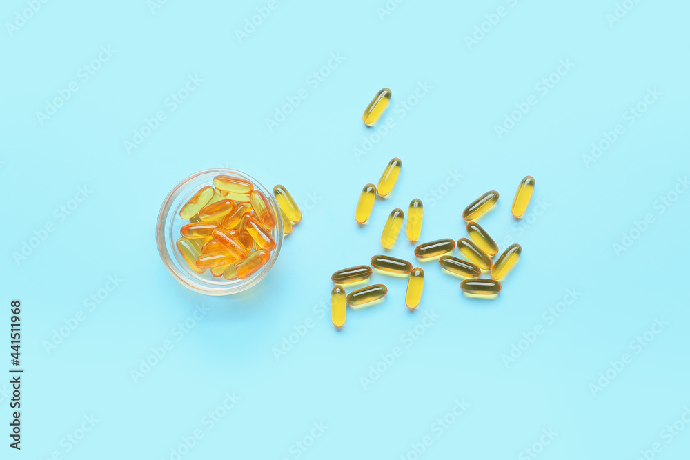 Bowl with fish oil capsules on color background