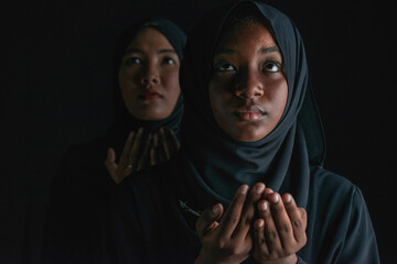 Wall Mural - African and Asian Muslim  woman in black hijab, Multiethnic Muslim women dressed in black hijab national wear, doing prayers on black background