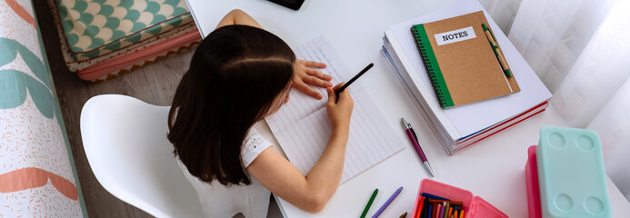 Wall Mural - Top view of unrecognizable girl doing homework sitting at a desk in her bedroom