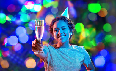 birthday, celebration and nightlife concept - happy smiling young african american woman in party cap with glass of champagne in ultraviolet neon lights over bokeh background