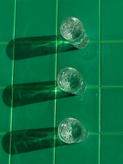 Wall Mural - Refreshing summer drinks in crystal glasses on green bar tile background reflection harsh shadow. Cold gin vodka cocktail for hot summer day. Non alcoholic soda clear water mint tonic. Party vacation