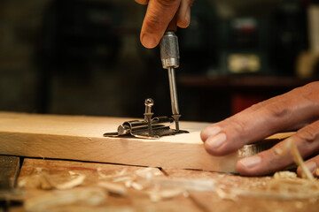 Carpenter screwing metal chrome hinges on wooden plank in the workshop.	