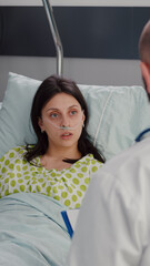 Closeup of sick woman with nasal oxygen tube resting in bed. Patient discussing with practitioner doctor about medical healdcare expertise checking disease test results working in hospital ward