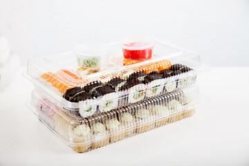 Two plastic boxes with sets of rolls, wasabi and ginger on a white plate.