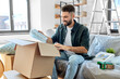 © Syda Productions - moving, people and real estate concept - happy smiling man unpacking boxes at new home