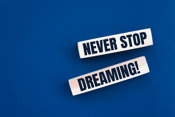 Poster - Never stop dreaming words printed on wooden blocks on blue. Positive thinking mindset concept