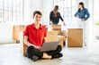 Young woman at laptop while moving home - Businesswoman working on portable device while setting up new office cardboard boxes and colleagues behind her Concept of start-up and new business activity