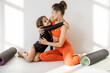 Sports mom and little daughter hug while sitting together with yoga mats during sports activities indoors. Close relationships with mother and sports in childhood
