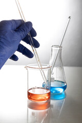 vertical image of lab assistent who holding glass pipette,two glass flasks on the table