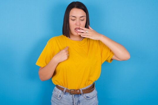 Shocked young beautiful brunette girl with short hair standing against blue background look surprisedly down, indicates at blank  with fore finger, Scared model