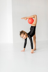 Little girl practising rhythmic gymnastic with a ball at white room. Children's gymnastics and training from an early age