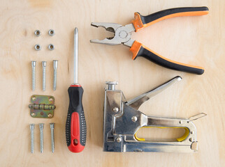 screwdriver, pliers, stapler and bolts on a wooden background.Construction tools