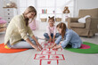 © New Africa - Mother and little girls taping sticker hopscotch on floor at home