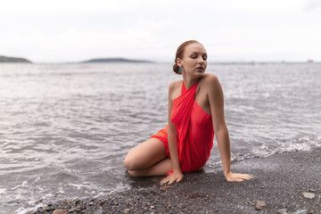 Wall Mural - Beautiful woman in a red dress on a beach.