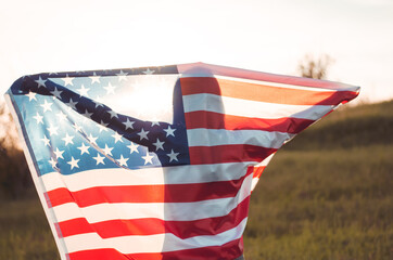 A young woman holds the US national flag in a field at sunset. 4th of July, Independence day. American freedom concept. Selective focus