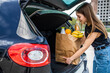 Beautiful young woman loading groceries into trunk of her car