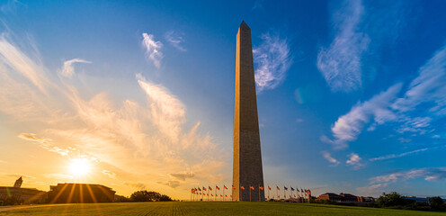 Sunrise behind the Washington Monument surrounded by a ring of American flags on the national mall in the United States capitol with Smithsonian Museums in background