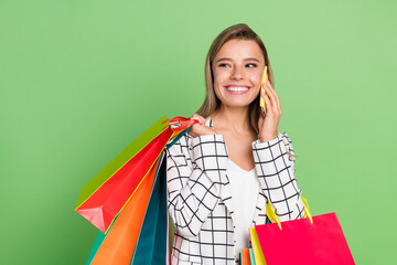 Portrait of attractive trendy cheerful girl carrying bags calling cellular isolated over bright green color background