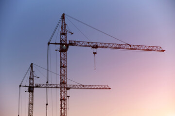 Silhouettes high rise cranes against blue pink sunset sky.