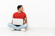 Caucasian handsome man with a laptop sitting on the floor in lateral position