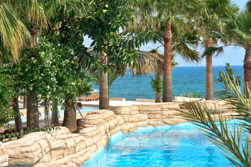 Tropical pool with beautiful palm trees and thatched umbrellas against the backdrop of the sea. Vacation concept, travel. Beautiful landscape