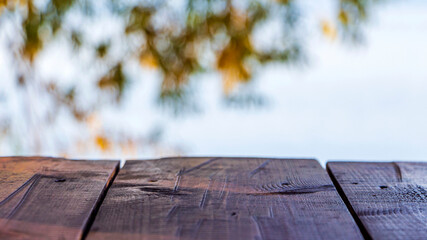 Empty wooden table in nature outdoors. Natural template mock up for display of product. Blur orange and yellow trees leaves in sunny autumn day