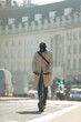 © Paul Bradbury/Caia Image - Businessman in face mask riding electric push scooter on city street