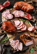 Assortment of cold meats products, ham, sausage, salami, parma, prosciutto, bacon on wooden cutting board with herb and spices over dark background. Meat appetizer, set of wine, top view