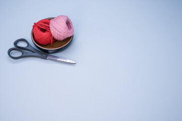 Sticker - Closeup shot of yarns for knitting and scissors in a wooden bowl on a blue background