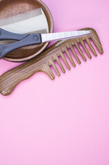 Poster - Vertical shot of hairbrushes, scissors, and a wooden bowl on a pink background