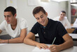 © liderina - Exam.  Teenagers students sitting in the classroom and writing. Focus is on foreground.