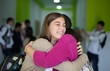 © liderina - Two best friends in high school.  Two girls hug. Students standing in school hallway. Focus is on foreground.