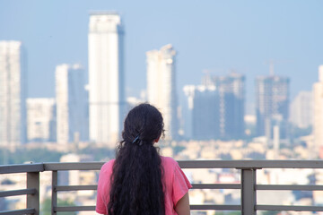 Zoomed in shot of indian woman with long hair in front of huge towers skyscrapers buildings with offices homes and shopping malls in gurgaon showing the real estate and property 