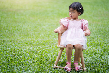 Wall Mural - Adorable little Asian girl sitting on wooden chair at field