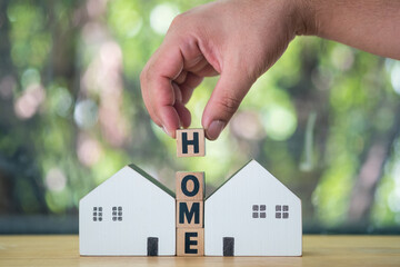 Wall Mural - The hand puts a wooden cube with the letter H from the word HOME between two home. Banking, real estate, Property investment