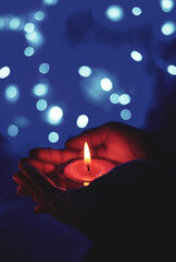 Wall Mural - Burning candle in the hands of a girl with bokeh light. Christmas candles. Candlelight glowing in woman's hands. Praying, faith, religion concept.