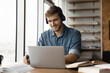 © fizkes - Smiling young handsome man in wireless headphones listening educational webinar lecture on computer, writing notes, improving professional knowledge, studying on online courses in modern home office.