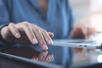 Wall Mural - Close up of woman hand using digital tablet, finger touching on screen and working on laptop computer on table at home office