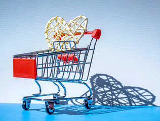 braided heart in red Mini shopping trolley for shopping with shadow on blue background, consumer concept, minimalism