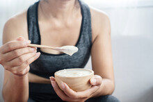 a healthy woman in sportswear eating yogurt after doing sport hand holding bowl and spoon closeup