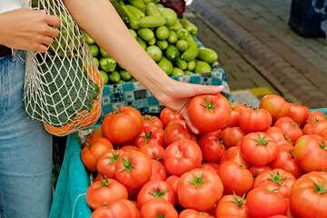 Wall Mural - Plant based diet concept. Young woman with reusable eco friendly net bag picking fresh tomatoes on farmers market. Conscious shopping for organic local vegetables. Close up, copy space, background.