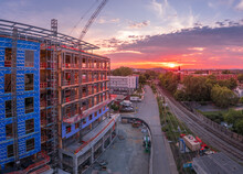 Aerial View Of Office Building, Apartment Complex Construction Site In Downtown Charlottesville Virginia With Red Cranes Standing Still Against The Setting Sun That Paints The Sky Red, Yellow, Orange 