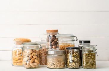 Glass jars with different products on light wooden background