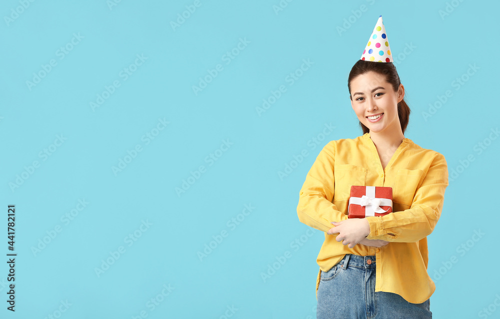 Young woman in party hat with gift box on color background