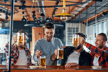 Canvas Print - Happy young men in casual clothing toasting each other with beer and smiling