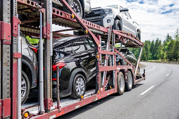 Car hauler big rig semi truck transporting cars on modular semi trailer running on the winding road