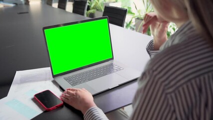 Wall Mural - Young Caucasian businesswoman ceo executive manager using typing email letter using laptop computer with empty blank green mockup screen for advertising at desk. Business concept. Over shoulder view.