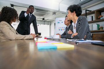 Successful African American businessman in formal clothing leading his team hopw to achieve business goal. Multiethnic busines team in a round table  meeting.